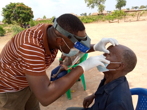 A surveyor in DRC uses the integrated loupe-shield to examine a man's eyes for trachoma.