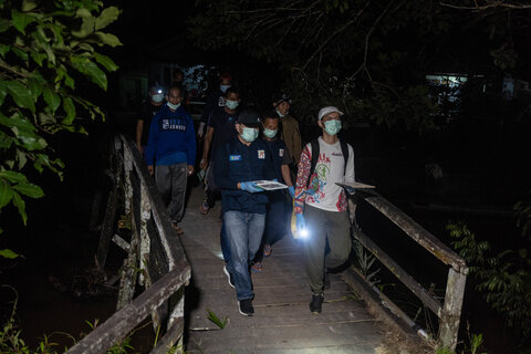 A team of health workers cross a bridge late at night wearing headlamps, they are going house to house to administer a survey for lymphatic filariasis. 