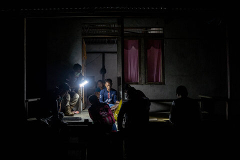 A family sits with health workers on the porch of their home in Indonesia late at night. Health workers wearing head lamps prick the finger of an individual to gather a blood sample as part of the survey for lymphatic filariasis. 